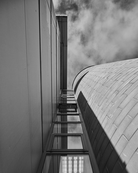 Upward view of modern building facades with curved and linear architectural elements against a cloudy sky.