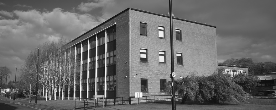 Modernist brick building with vertical column supports and regular window grid photographed in black and white.