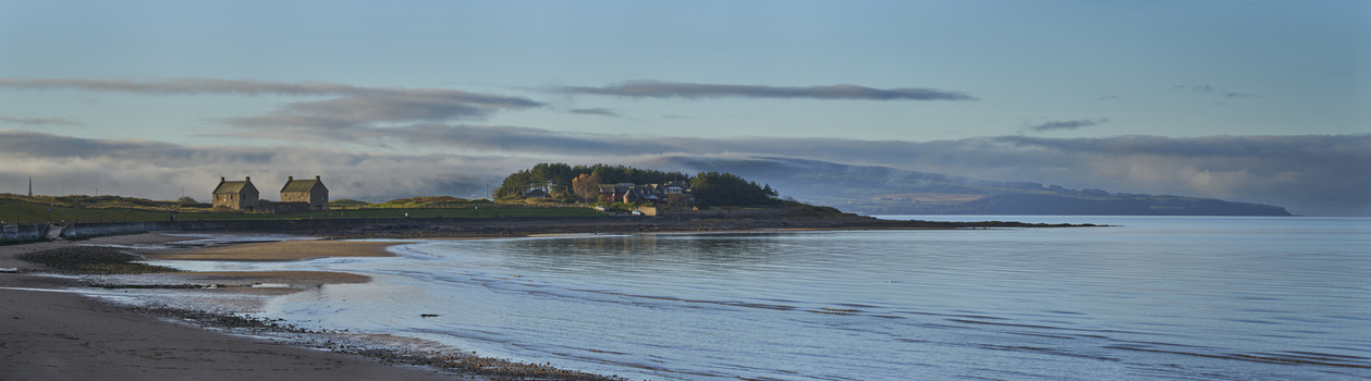 Coastal landscape with stone cottages on a headland overlooking a calm bay at golden hour.