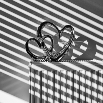 Decorative metal scissors with intertwined handles casting sharp shadows on a striped and checkered surface.
