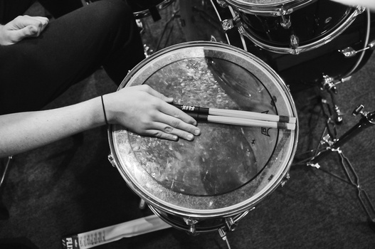 Drummer's hands holding stick over snare drum in black and white overhead view.
