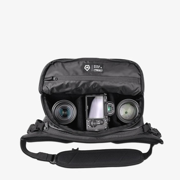 Camera bag opened to reveal organized compartments holding a DSLR body, two lenses, and accessories.