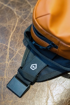 Tan leather camera bag with navy blue strap and buckle on textured surface.
