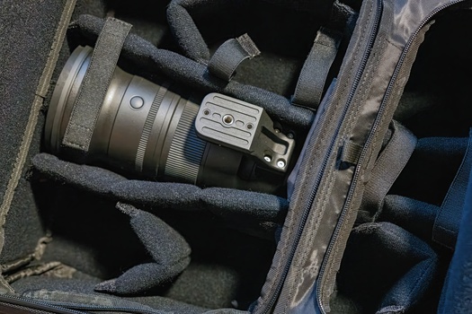 Camera lens and accessory packed in protective foam inside a gray camera bag.
