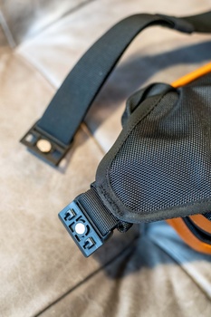 Close-up of camera bag straps and attachment points on neutral fabric surface.