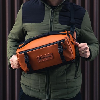 Person holding an orange and black camera bag with multiple compartments and straps.