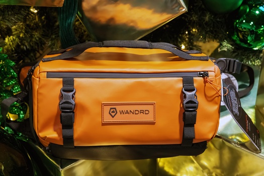 Bright orange WANDRD duffel bag with black straps and branded label displayed indoors with warm lighting.