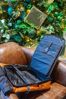 Travel bags and accessories arranged on a brown leather surface with holiday decorations in background.