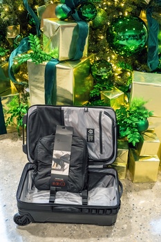 Open rolling suitcase displaying camera gear and accessories with wrapped gift boxes in background.
