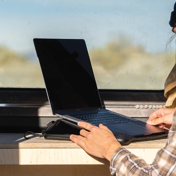 Photographer's hands working on laptop at outdoor desk with natural daylight and blurred landscape background.