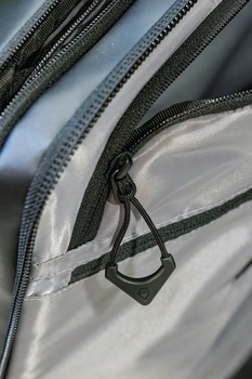 Close-up of black nylon zipper pulls and cords on white fabric with gray ribbed webbing straps.