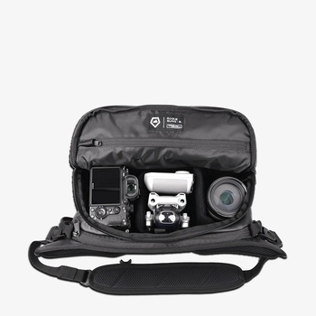 Overhead view of an open camera gear bag displaying a drone, camera body, and telephoto lens inside custom compartments.