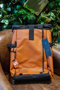 Orange and black weatherproof camera backpack with compression straps and side pockets displayed outdoors.