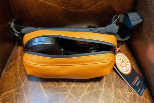 Orange camera bag with blue-grey strap open to reveal compact camera and accessories inside.