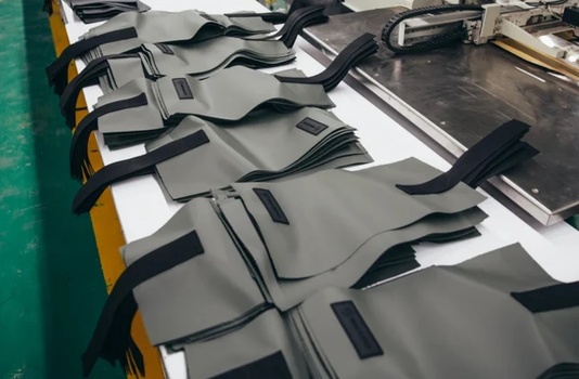 Row of gray car floor mats with black trim laid out on white surface next to green wall.