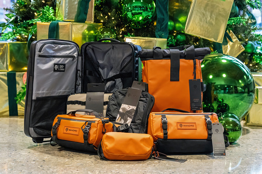 Collection of orange and black camera bags and cases arranged on concrete with green decorative backdrop.