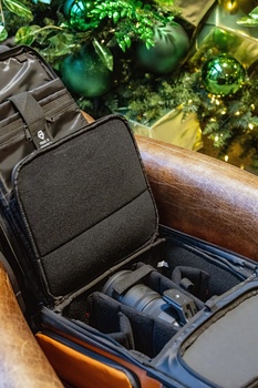 Black camera bag with lenses and gear organized inside, displayed in an open car trunk among green foliage.