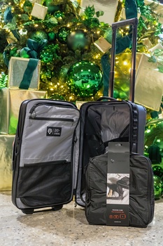 Two open travel luggage cases displayed against a decorated Christmas tree backdrop with gold ornaments and garland.