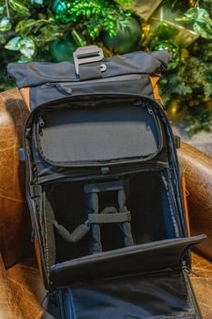 Open camera backpack displaying interior compartments with camera body and lens storage against green foliage background.