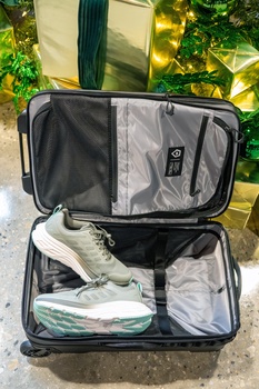 Open suitcase with packed clothing and shoes, viewed from above on concrete ground with foliage in background.