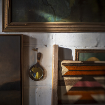 Framed landscape painting above a wooden shelf holding vintage books and a brass compass.