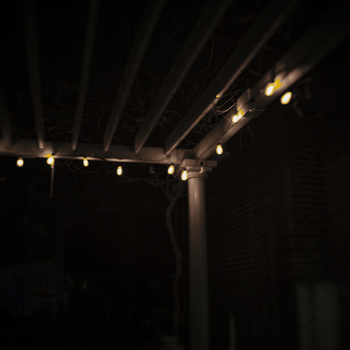 Overhead pergola with warm string lights creating golden bokeh against dark night sky.
