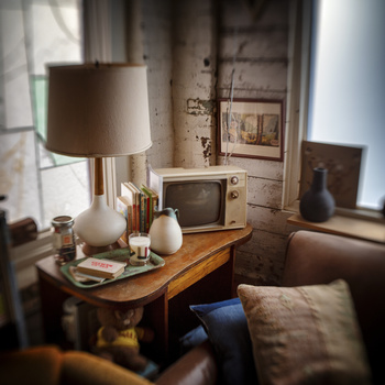 Warm-toned interior scene featuring a wooden side table with table lamp and decorative objects near a window with natural light.