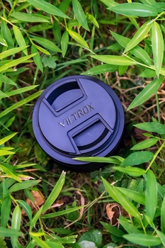 Purple lens cap with center pinch design resting on grass and soil.