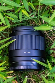 Telephoto camera lens with ribbed barrel resting on green grass and foliage.