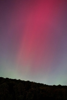 Gradient sky transitioning from pink and magenta at top to green and gray near dark hillside silhouette.