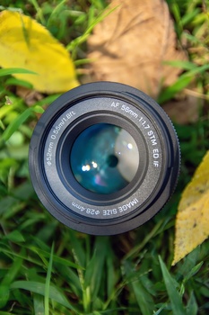 Vintage camera lens with blue-tinted glass elements, mounted on grass and autumn leaves.