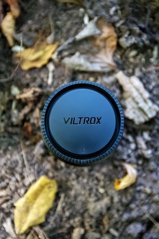 Viltrox lens filter cap placed on textured ground with fallen leaves and moss.
