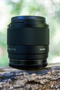 Black telephoto lens with vertical ridged grip and visible focal length markings resting on weathered tree bark.