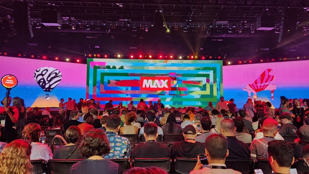 Large conference stage with colorful neon lighting and MAX branding, audience seated in foreground.
