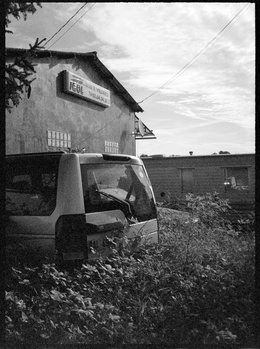 Abandoned truck cab beside a rural building under overcast sky.