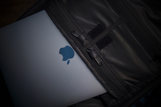 MacBook laptop with illuminated Apple logo visible inside a black camera bag or case.