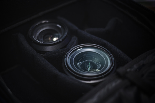 Two camera lenses mounted on a dark camera body, photographed from above with dramatic side lighting.