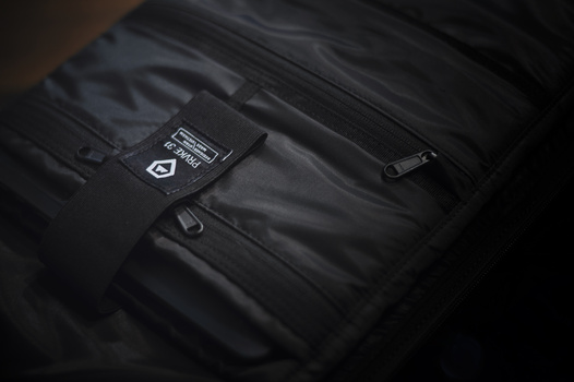 Close-up of black technical jacket with utility pockets and branded label detail.