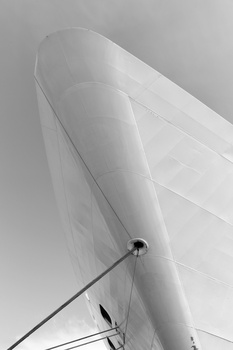 White sail billowing against overcast sky, shot from below with mast and rigging visible.