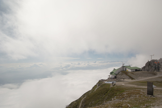 Mountain lodge on a ridge overlooking a sea of clouds beneath overcast sky.