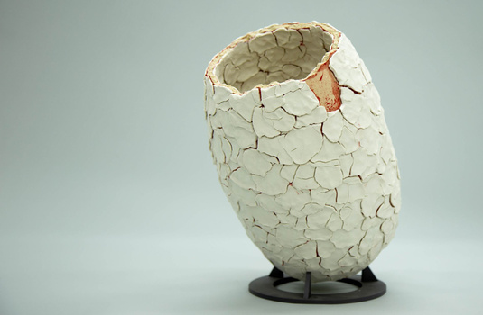 Cracked white eggshell with opening at top, mounted on black base against neutral gray background.