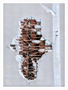 Aerial view of a snow-covered cross made from stacked wooden logs on white ground.