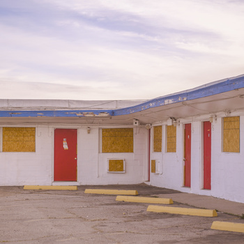 Modernist motel facade with bright pink door and red accent doors against white walls under blue roof.