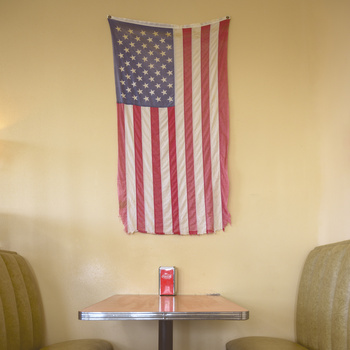 American flag tapestry hanging on a pale yellow wall above a small table with two chairs.