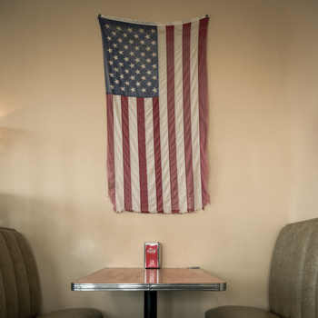 Faded American flag tapestry hanging on a beige wall above a small table with two chairs.