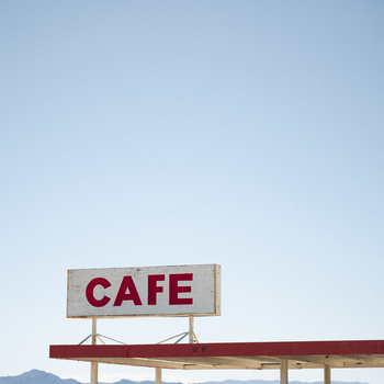 Vintage roadside cafe sign with red lettering against clear blue sky and desert landscape.