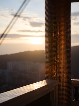 Warm golden light from sunset illuminates a brick column in the foreground, with mountains and valley visible in the soft-focused background.