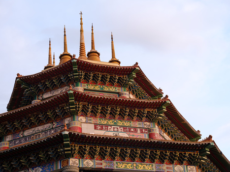 Ornate Asian temple roof with multiple tiers, upturned eaves, and golden spires against a cloudy sky.