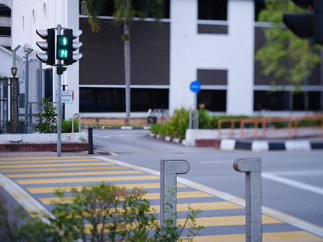 Yellow pedestrian crossing with green traffic light and modern building in soft focus background.