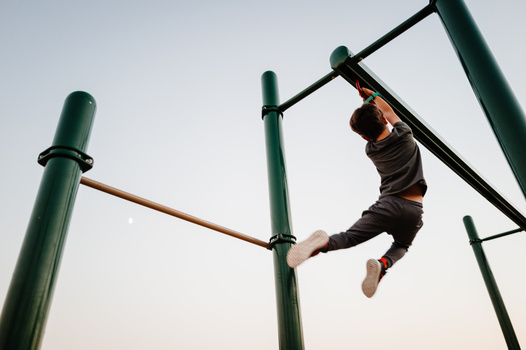 Young person mid-swing on outdoor monkey bars against a clear sky.